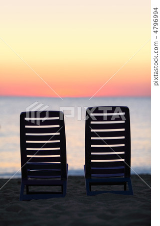 Two empty chairs stand on sand near sea during sunset Two empty chairs stand on sand near sea during sunset 4796994