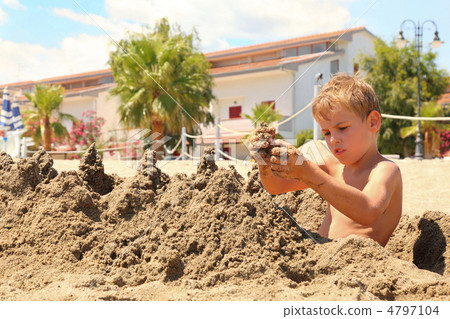 Boy on  beach sits and models hills from wet sand 4797104