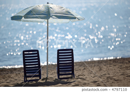 Two dark blue empty chairs  stand on  beach near  sea under shad 4797110