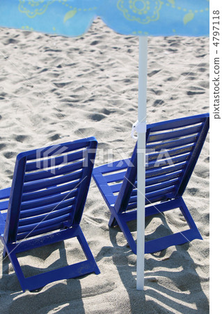 Two dark blue plastic chairs stand on  beach under  umbrella 4797118