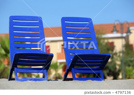 Two empty dark blue chairs stand on sand under sun Two empty dark blue chairs stand on sand under sun 4797136