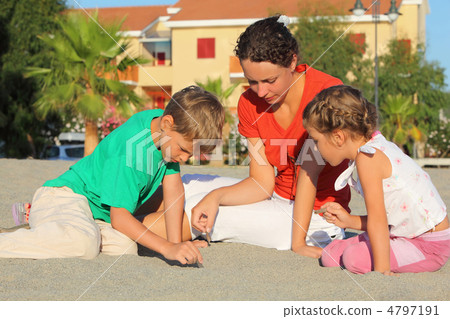 Mother with two children sit on  beach and draw on sand 4797191