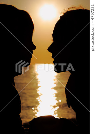 Silhouettes of mother and son in evening at seaside  during suns 4797221