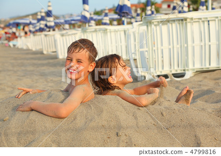 little brother and sister buried in sand on beach, rows of white 4799816