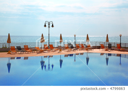 few orange loungers and parasol standing near to open pool, sea 4799863