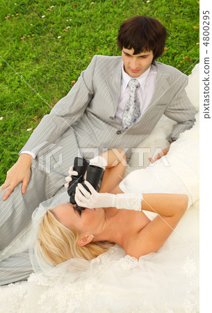 Beautiful young groom and bride wearing white dress lie on green Beautiful young groom and bride wearing white dress lie on green 4800295