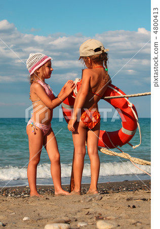 two little sisters in swimsuits standing on beach near metal pol 4800413