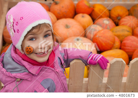 Little girl with tattoo on cheek costs near big box with pumpkin 4801673