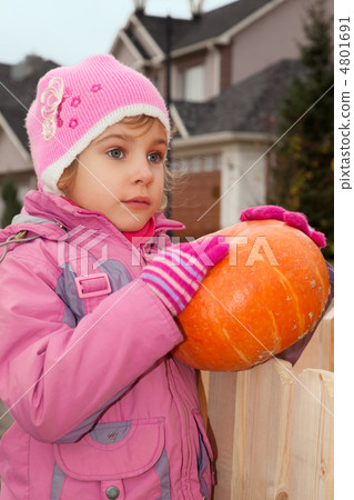 little girl stands in court yard of house and holds pumpkin little girl stands in court yard of house and holds pumpkin 4801691