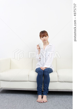 A woman sitting on a couch and relaxing while drinking coffee A woman sitting on a couch and relaxing while drinking coffee 4975737