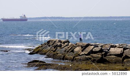 Rocky breakwater with young man and with a boat in the backgroun Rocky breakwater with young man and with a boat in the backgroun 5012890