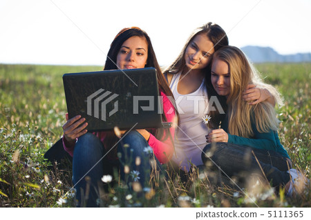 three young beautiful woman with a laptop sitting in the field o three young beautiful woman with a laptop sitting in the field o 5111365