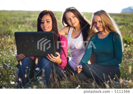 three young beautiful woman with a laptop sitting in the field o three young beautiful woman with a laptop sitting in the field o 5111366