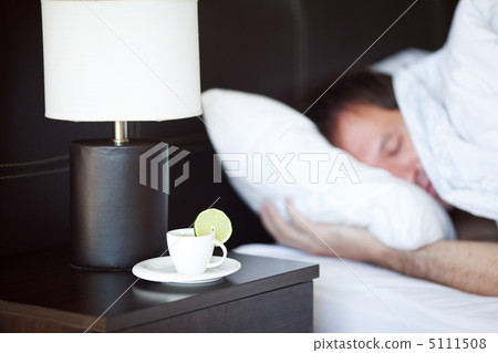 man sleeping on a bed, a cup of tea on the bedside table and lam 5111508
