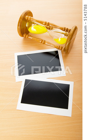 Blank instant photos and hour glass on the wooden table 5143788
