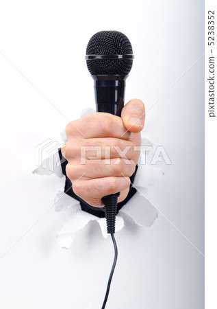 Hand holding microphone through hole in paper Hand holding microphone through hole in paper 5238352