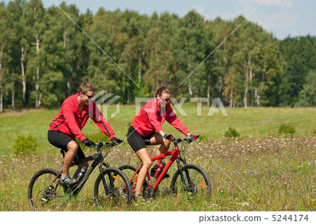 Young couple riding mountain bike in spring meadow Young couple riding mountain bike in spring meadow 5244174