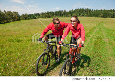 Young couple riding mountain bike in spring meadow Young couple riding mountain bike in spring meadow 5246032
