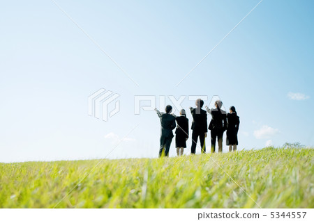A businessman and a businesswoman pointing at the fingers standing in the meadow and the back of the business woman 5344557