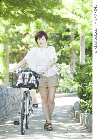 A woman walking by pushing a bicycle 5477843