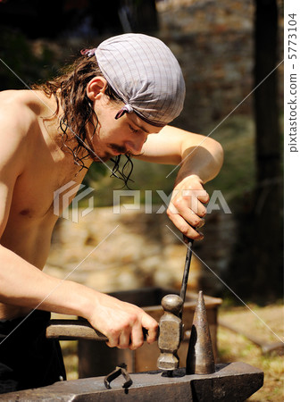 Young blacksmith hammering hot iron on anvil Young blacksmith hammering hot iron on anvil 5773104
