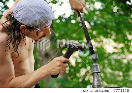 Young blacksmith hammering hot iron on anvil Young blacksmith hammering hot iron on anvil 5773156