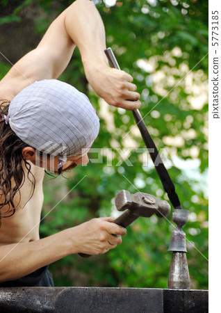 Young blacksmith hammering hot iron on anvil Young blacksmith hammering hot iron on anvil 5773185