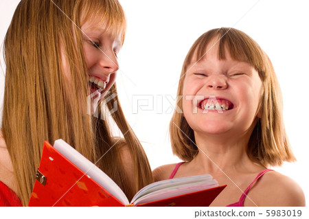 Two little girls looking like sisters holding red book, laughing 5983019