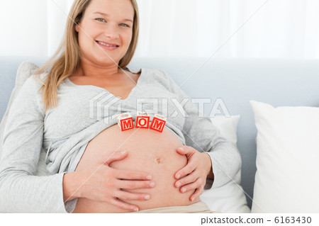 Blond pregnant woman with mom letters on her belly lying on a be 6163430