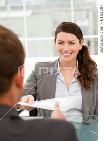Happy businesswoman giving a paper to a male colleague during a 6163887
