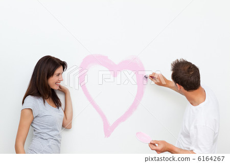 Cute woman looking at her boyfriend painting a heart Cute woman looking at her boyfriend painting a heart 6164267