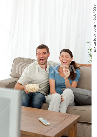 Cute couple eating pop corn while watching television on the sof Cute couple eating pop corn while watching television on the sof 6164559
