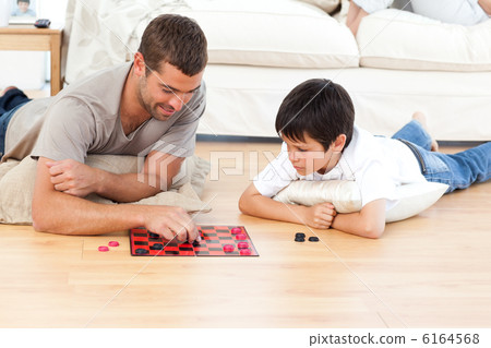 Handsome man playing checkers with his son lying on the floor Handsome man playing checkers with his son lying on the floor 6164568
