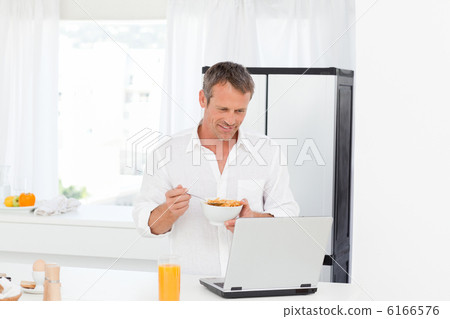Man eating cereal while he is working on his laptop Man eating cereal while he is working on his laptop 6166576