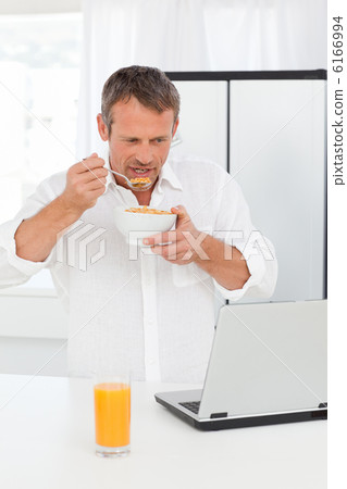 Man eating cereal while he is working on his laptop Man eating cereal while he is working on his laptop 6166994