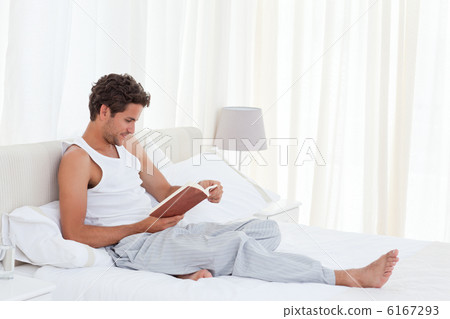 Man reading a book on his bed Man reading a book on his bed 6167293