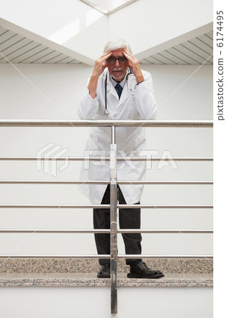 Stressed doctor  leaning on  railing with hands on forehead in h 6174495