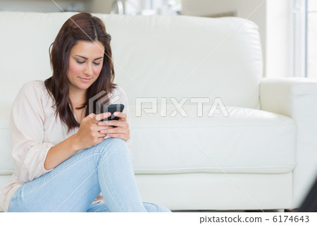Brunette texting with mobile phone on the floor Brunette texting with mobile phone on the floor 6174643