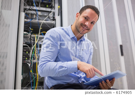 Happy technician working on tablet pc beside servers Happy technician working on tablet pc beside servers 6174905