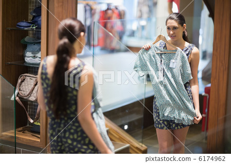 Woman is looking in the mirror while holding up clothes 6174962