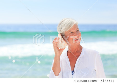 Mature woman listening to her shell 6185344