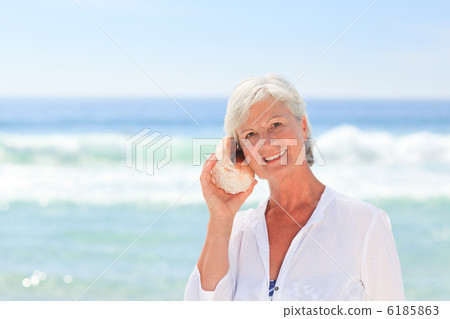 Mature woman listening to her shell 6185863