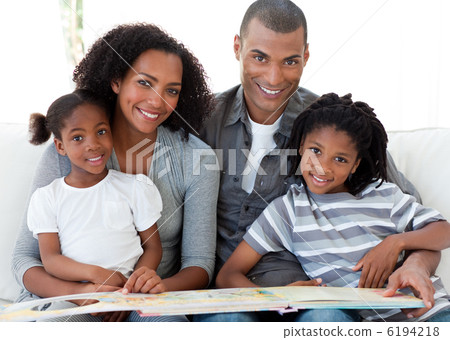 Portrait of an Afro-American family reading a book in the living 6194218