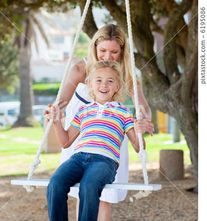 Jolly mother pushing her daughter on a swing 6195086