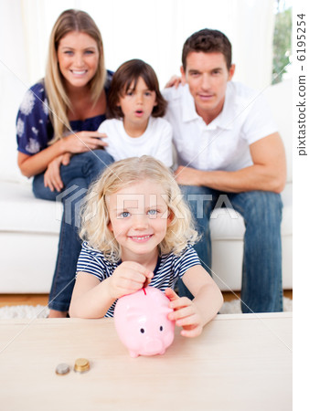 Blond little girl inserting coin in a piggybank Blond little girl inserting coin in a piggybank 6195254