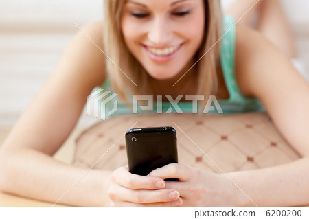 Smiling blond woman sending a text lying on the floor 6200200