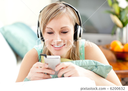 Smiling blond woman listening music lying on a sofa Smiling blond woman listening music lying on a sofa 6200632