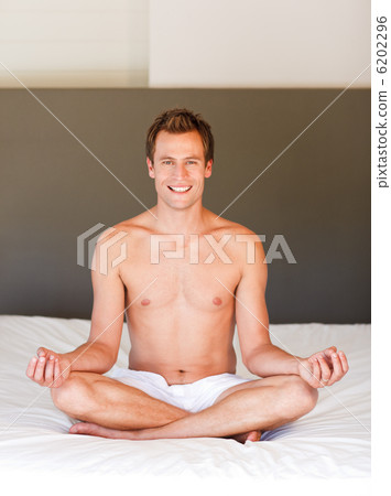 Smiling handsome man meditating on bed Smiling handsome man meditating on bed 6202296