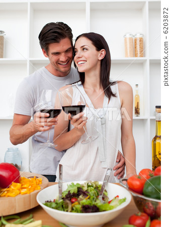 Smiling couple drinking wine and preparing a salad Smiling couple drinking wine and preparing a salad 6203872