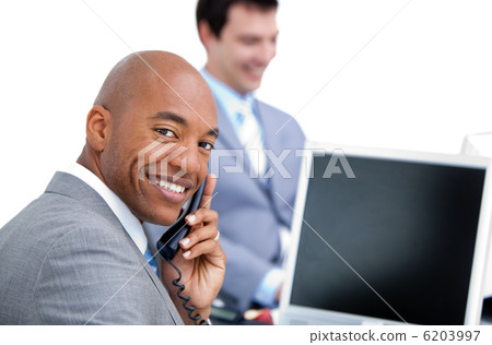 Happy businessman on phone and his colleague working at a comput 6203997